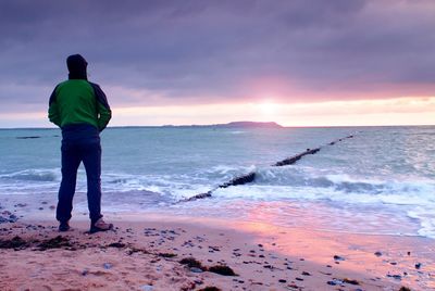 Man silhouette stand alone on stony beach and watching romantic colorful sunrise