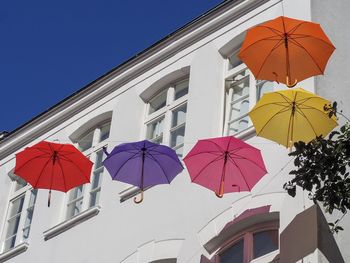 Low angle view of umbrellas against building against clear blue sky