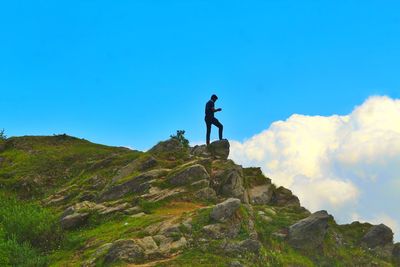 Low angle view of man standing on rock against sky