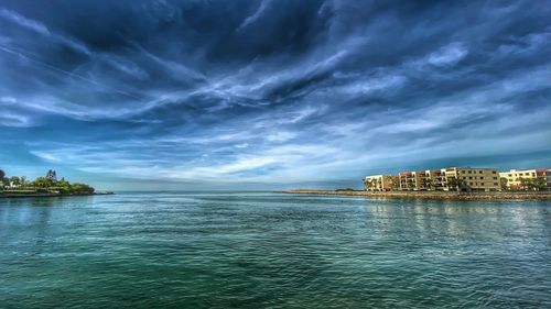 View of buildings by sea against cloudy sky