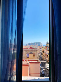 Buildings seen through glass window against clear blue sky