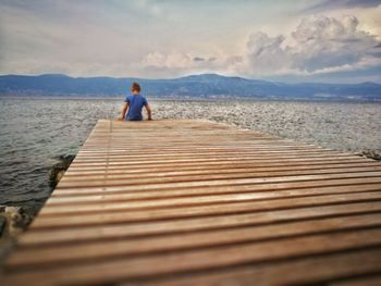 Man standing on jetty by lake against sky