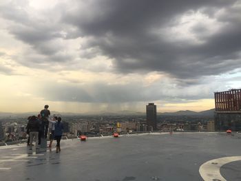 People walking on city street against cloudy sky