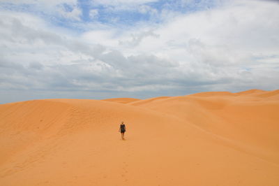 Scenic view of woman walking in desert against sky