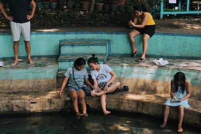 Full length of friends sitting on swimming pool