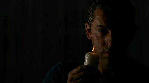 Close-up portrait of man holding illuminated candle against black background