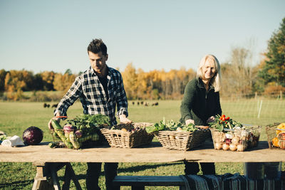 Male and female farmers arranging organic vegetables for sale on table