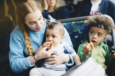 Mother feeding baby boy while sitting with son in bus