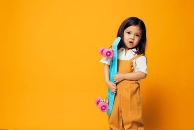 Portrait of smiling young woman standing against yellow background