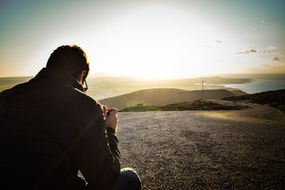 Rear view of woman sitting on landscape against sky