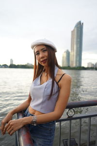 Portrait of woman standing against river in city