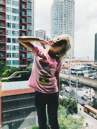 Full length of smiling young woman standing against buildings in city