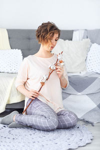 Woman sitting on sofa at home with cotton twig