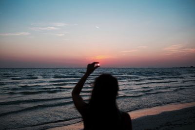 Optical illusion of woman holding sun at beach against sky during sunset
