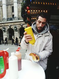 Man putting mustard on hot dog while standing at sidewalk cafe