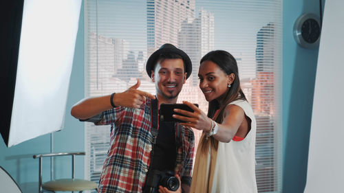 Portrait of smiling young woman using phone while standing in office