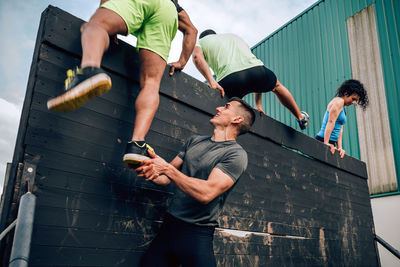 Young man assisting friend while climbing wooden wall