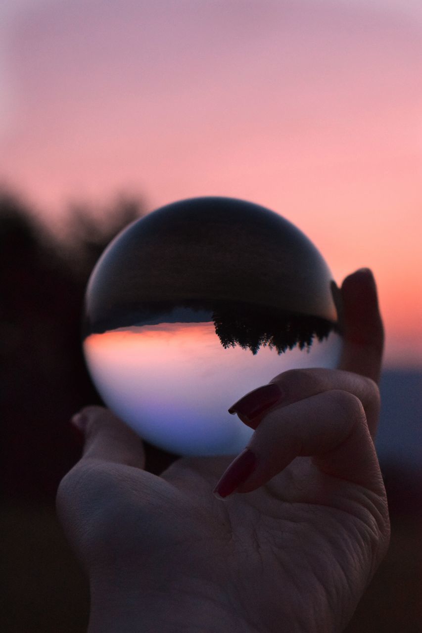 CLOSE-UP OF HAND HOLDING CRYSTAL BALL AGAINST SKY