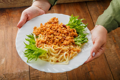 A plate of pasta in bolognese sauce in female hands. horizontal photo