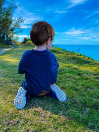 Rear view of boy sitting on field against sky