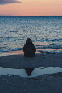 Rear view of woman sitting on beach against sky during sunset