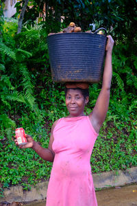 Portrait of woman holding pink while standing against plants