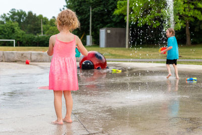 Small children playing with water and toys at fountain splash pad in park in summer. 