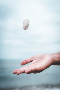 Close-up of hand catching stone against sea and sky