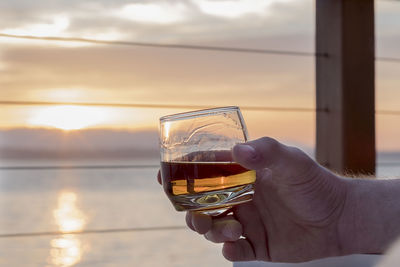 Close-up of hand holding drink at sunset