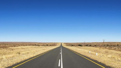 Road leading towards landscape against clear blue sky