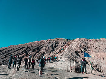 Group of people on land against clear blue sky