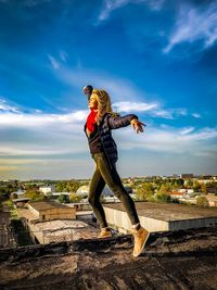 Woman dancing on building terrace against sky in city