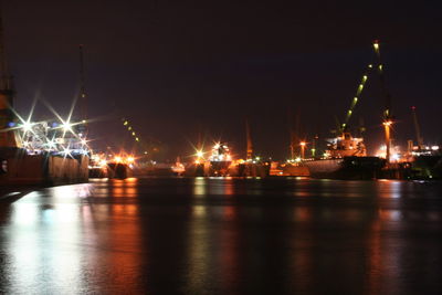 Illuminated city by sea against sky at night