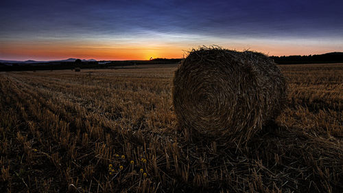 Hay bales on field against sky at sunset