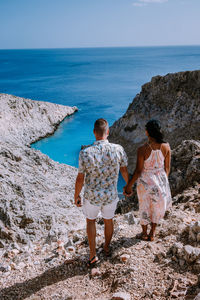 Rear view of couple standing on rock by sea against sky