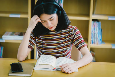 Young woman reading book while listening music on table