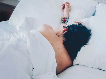 Rear view of shirtless woman relaxing on bed at home