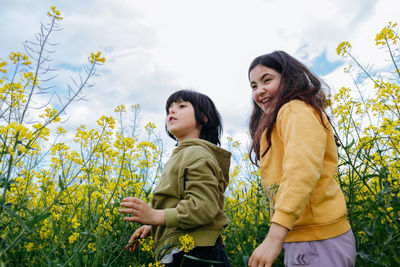 Low angle view of two children standing in the field of yellow flowers against blue sky