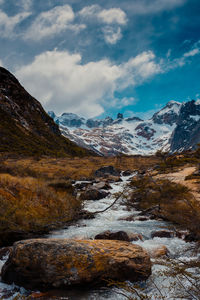 Scenic view of stream by snowcapped mountains against sky