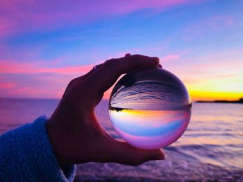 Close-up of hand holding crystal ball at beach against sea during sunset