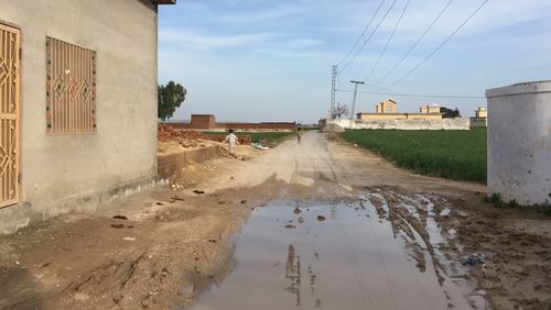 Wet road by puddle against sky