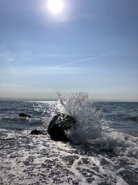 Sea waves splashing on shore against sky