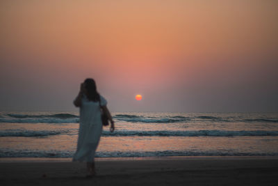 Silhouette woman standing at beach during sunset