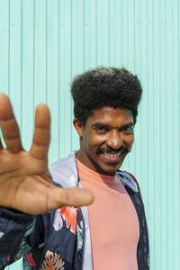 Afro man showing hand in front of turquoise wall during sunny day