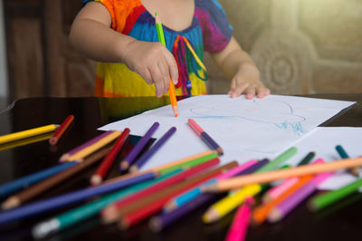 Midsection of woman with multi colored pencils on table