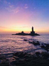 Silhouette lighthouse by sea against sky during sunset