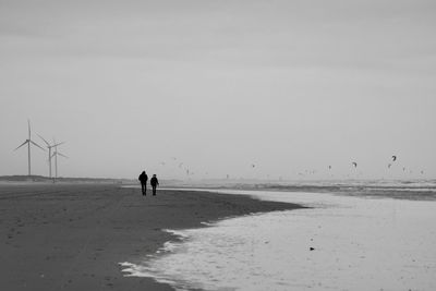 Rear view of couple walking on beach against sky