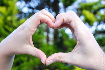 Cropped image of hands making heart shape against trees