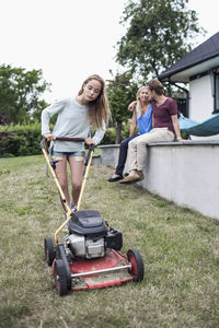 Girl mowing lawn with parents sitting in background at yard