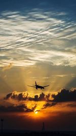 Silhouette airplane flying over sea against sky during sunset